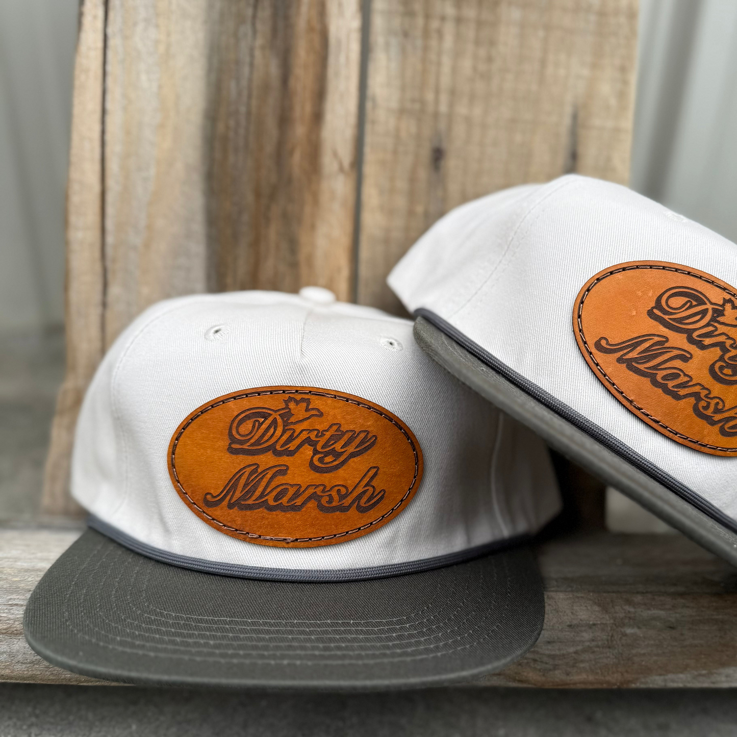 White Goat Rope hat with a dark gray brim and an oval brown leather "Dirty Marsh" patch.