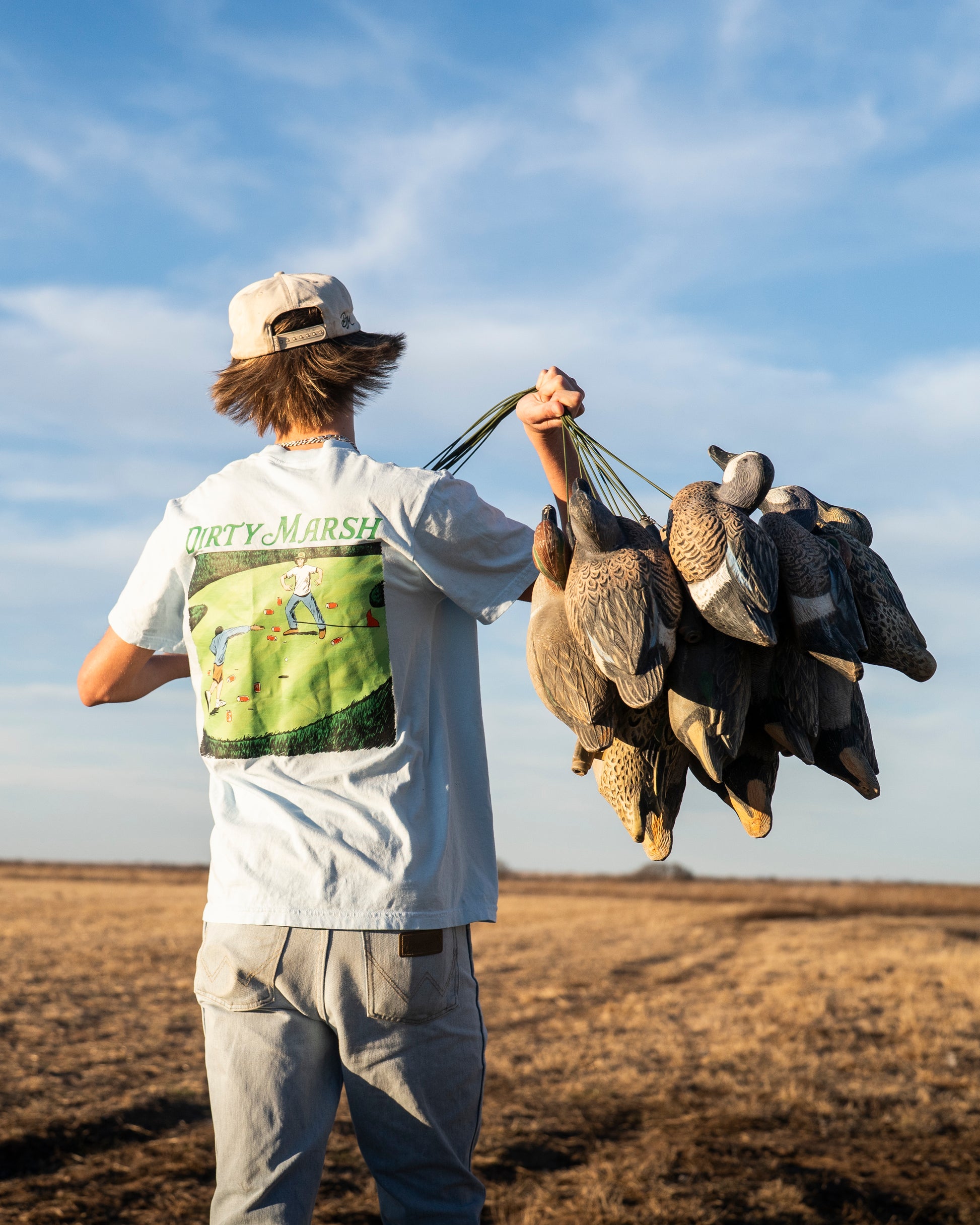 Person holding dead birds in a field with a blue sky