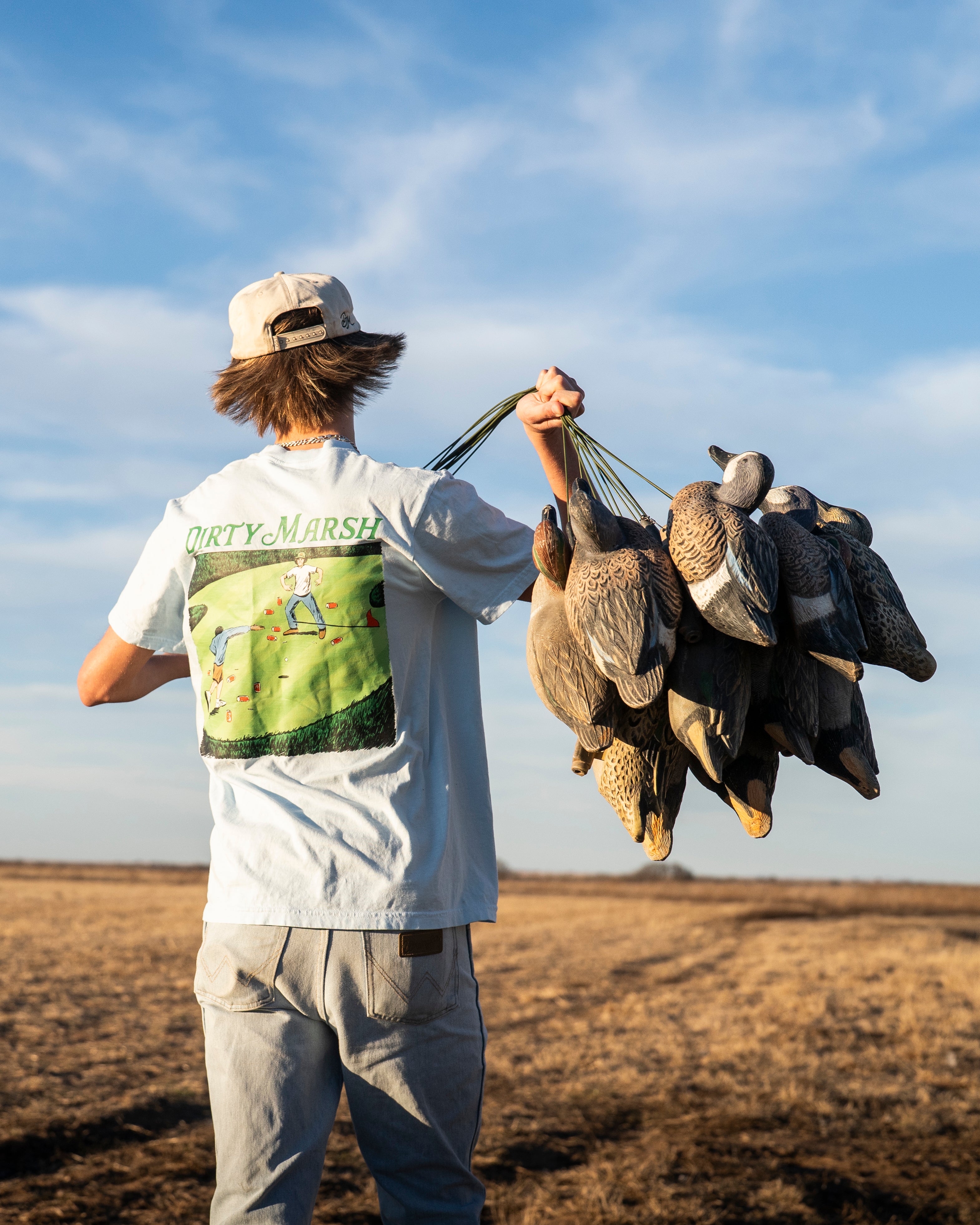 Person holding dead birds in a field with a blue sky