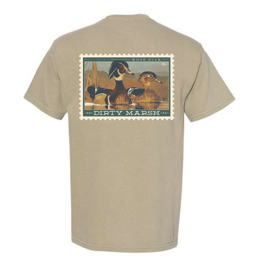 A Comfort Colors Wood Duck Stamp Tee in Sandstone that says Dirty Marsh.