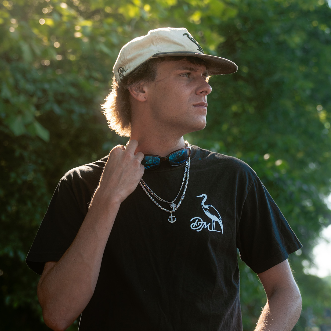 Person wearing a black t-shirt with a logo, standing outdoors with greenery in the background